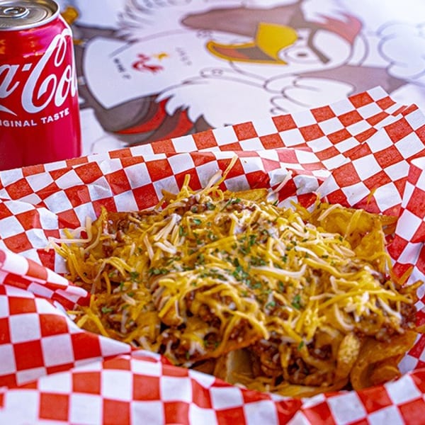 Chili cheese fries in a red and white checkered basket with a Coca-Cola can beside it.