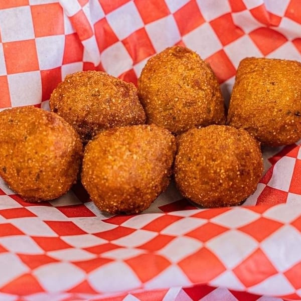 Six golden-brown hush puppies rest in a red and white checkered paper-lined basket.