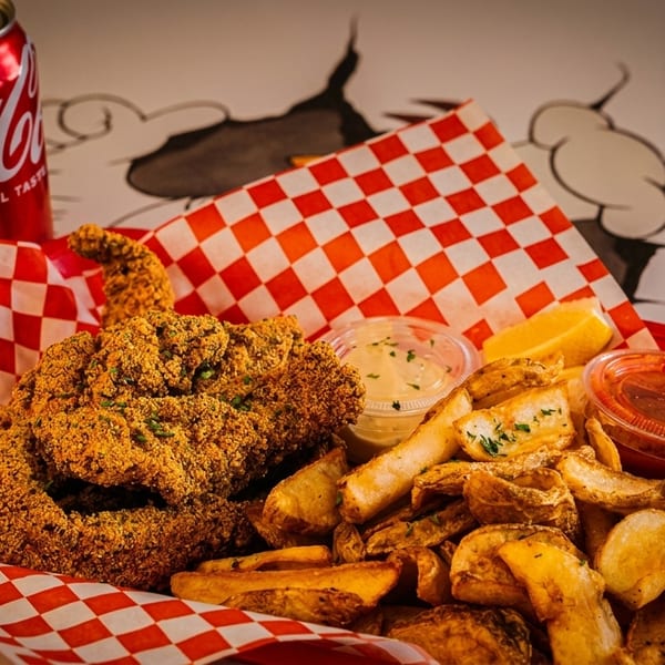 Fried fish and potato wedges in a red basket with sauces and a Coca-Cola can.