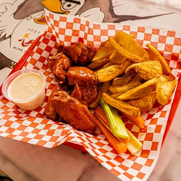 A red basket with checkered paper holds buffalo wings, potato wedges, celery, carrots, and ranch dressing.