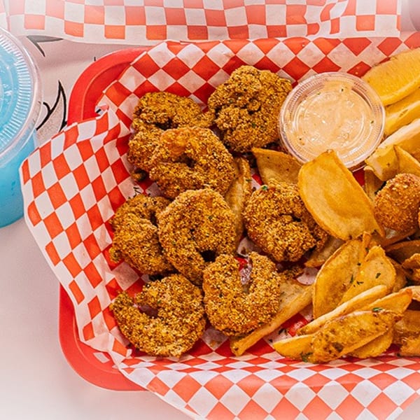 Fried shrimp, potato wedges, and hush puppies in a red basket with a blue drink.