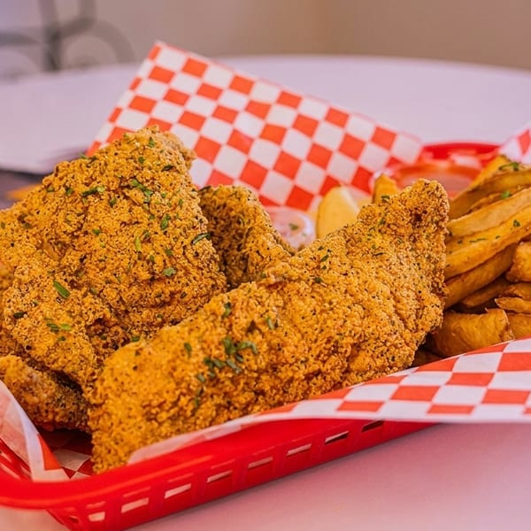 Crispy fried fish fillets and golden french fries served in a red basket with checkered paper.